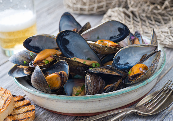 A bowl of delicious steamed mussels with grilled bread and beer on a rustic tabletop with fish net.